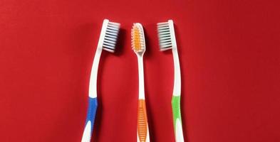 trois brosses à dents de couleurs différentes isolées sur fond rouge. vue de dessus photo