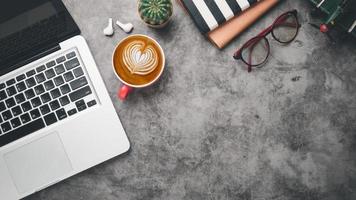 lieu de travail de bureau avec ordinateur portable, écouteurs, lunettes, cahier et tasse de café, vue de dessus à plat avec espace de copie. photo