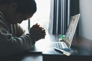 concept de technologie en ligne chrétienne. mains priant de chrétien avec ordinateur portable numérique, église en direct en ligne pour le service du dimanche. une femme catholique asiatique lit le livre de la sainte bible et étudie en ligne. photo