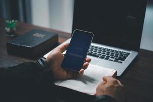 concept de technologie en ligne chrétienne. mains priant de chrétien avec ordinateur portable numérique, église en direct en ligne pour le service du dimanche. l'homme catholique asiatique lit le livre de la sainte bible et l'étude en ligne. photo