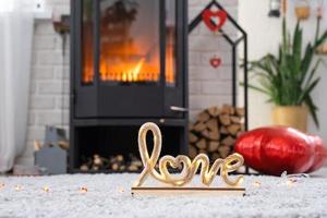 décor de saint valentin près d'un poêle à bois avec feu et bois de chauffage. foyer confortable à l'intérieur avec des plans en pot, saint valentin dans un nid d'amour familial. photo