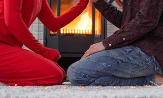 homme et femme amoureux à la maison sont assis près du poêle à bois avec un feu brûlant sur un tapis confortable. saint valentin, couple heureux, histoire d'amour, relations photo