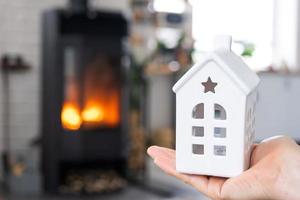 clé de la maison avec porte-clés dans la main du propriétaire contre le poêle à cheminée avec feu et bois de chauffage. foyer chaleureux. construction, conception, projet, déménagement dans une nouvelle maison, hypothèque, location et achat immobilier photo