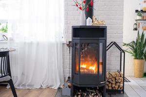 décor de saint valentin près d'un poêle à bois avec feu et bois de chauffage. foyer confortable à l'intérieur avec des plans en pot, saint valentin dans un nid d'amour familial. photo