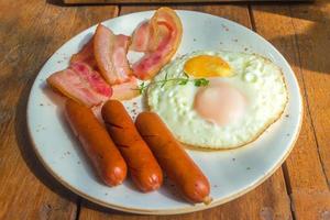 bacon, œufs au plat et saucisses sur plaque blanche et table en bois photo