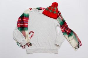 gros plan sur l'espace de copie de sweat-shirt de modèle vierge gris. concept de vacances de noël. sweat à capuche maquette vue de dessus, écharpe, chapeau. décorations de fêtes rouges sur fond blanc. accessoires de bonne année. tenue de Noël photo