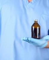 médecin en uniforme bleu et gants en latex tenant une bouteille en verre brun photo