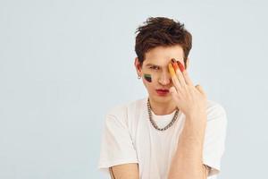 jeune homme gay est debout dans le studio et pose pour un appareil photo. peint par un maquillage multicolore photo