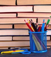 piles de divers livres cartonnés et verre de papeterie bleu avec des crayons en bois multicolores photo