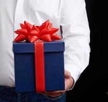 un homme en chemise blanche tient une boîte en carton cadeau bleue avec un arc rouge photo