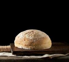 pain de blé blanc rond cuit au four sur une serviette textile, vieille table en bois photo