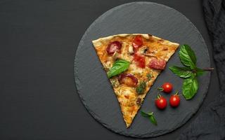 délicieuse tranche de pizza triangulaire avec saucisses fumées, champignons, tomates, fromage et feuilles de basilic photo