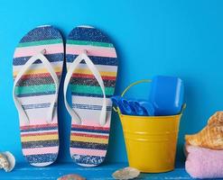 paire de chaussons de plage pour femmes, un seau jaune pour bébé et des coquillages éparpillés photo