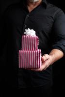 homme adulte dans une chemise noire tient dans sa main une pile de cadeaux emballés dans du papier photo