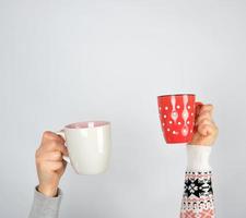 Deux mains dans un chandail tenant des tasses en céramique sur fond blanc photo