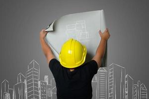 Jeune garçon portant un chapeau d'ingénieur jaune et des idées de plan de maison sur un tableau noir photo