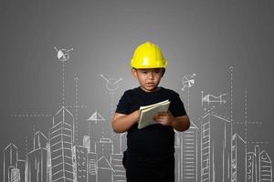 Jeune garçon portant un chapeau d'ingénieur jaune et des idées de plan de maison sur un tableau noir photo