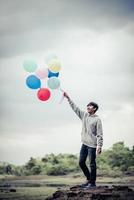 jeune homme tenant des ballons colorés dans la nature photo