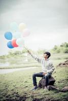 jeune homme tenant des ballons colorés dans la nature photo