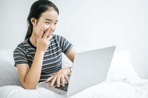 une jeune femme jouant sur son ordinateur portable au lit