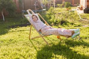 jeune femme en pyjama se repose sur une chaise sur une pelouse verte aux beaux jours d'été - vie de village et de campagne photo