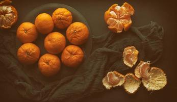 mandarines mûres rondes dans une assiette sur une serviette textile noire, vue de dessus photo