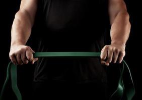 athlète avec un corps musclé en vêtements noirs fait des exercices physiques avec du caoutchouc vert photo