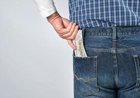 un homme vêtu d'une chemise à carreaux bleue et d'un jean met des dollars américains en papier dans sa poche arrière photo