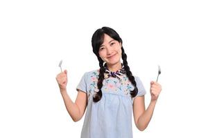 portrait de la belle jeune femme asiatique sourire en robe denim avec cuillère et fourchette sur fond blanc photo