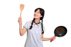 portrait d'une belle jeune femme asiatique portant une robe en jean avec une poêle noire et une spatule sur fond blanc isolé photo