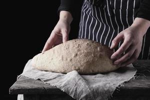 mains féminines tenant du pain de farine de blé cuit ovale sur une table en bois photo