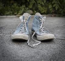 Paire de vieilles baskets en textile bleu usé sur asphalte gris photo