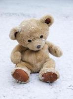 Le vieil ours en peluche est assis sur la neige blanche photo