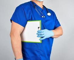 un médecin en uniforme bleu et des gants en latex stériles tiennent un presse-papiers photo