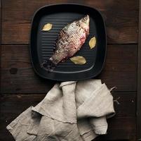 poisson carassin frais saupoudré d'épices et se trouve dans une casserole carrée noire, photo