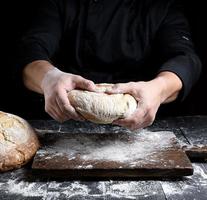 les mains du chef masculin tiennent une miche entière de pain rond cuit au four photo