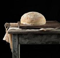 pain de blé blanc rond cuit au four sur une serviette textile, vieille table en bois photo