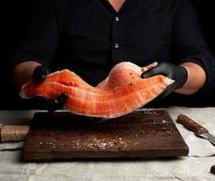 le chef en chemise noire et gants en latex noir tient un gros morceau de filet de poisson saumon sur la table photo
