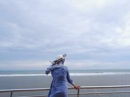 dos de la femme au chapeau sur la plage tropicale qui regardait le ciel et la mer depuis le pont. vue sur la mer photo
