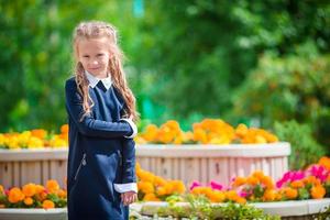 jolie petite fille souriante posant devant son école le premier septembre. adorable petit enfant très excité à l'idée de retourner à l'école photo