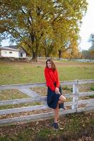 une belle fille dans un chandail rouge se tient près d'une clôture en bois blanche. bel automne chaud. photo