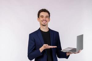 portrait d'un jeune homme d'affaires souriant et beau tenant un ordinateur portable dans les mains, tapant et parcourant des pages Web isolées sur fond blanc photo