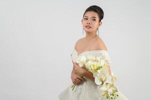 Jeune belle mariée asiatique avec bouquet d'orchidées sur fond blanc photo