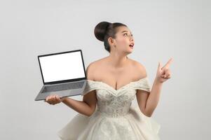 Jeune belle mariée asiatique pose avec un ordinateur portable maquette à la main photo