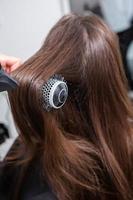 jeune femme peignant ses longs cheveux noirs avec un peigne dans un salon de beauté. une chevelure brune droite et saine qui a subi la procédure de lissage des cheveux. photo