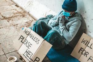 L'homme est assis à côté de la rue portant un masque médical avec un message de sans-abri photo