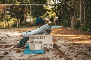 mendiant assis dans la rue avec des messages de sans-abri s'il vous plaît aider photo