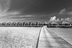 bungalow idyllique ou spectaculaire sur l'eau, îles maldives. processus noir et blanc dramatique pour la solitude ou l'inspiration. vue en perspective en mer depuis le centre de la jetée en bois ciel dramatique à la lumière du jour. photo