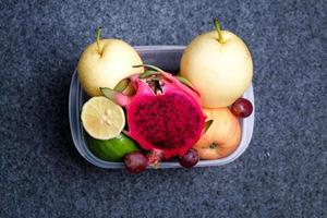 vue de dessus de tranches de fruits frais et entiers dans un récipient transparent sur fond sombre. concept d'aliments sains photo