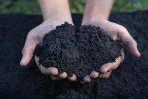 mains tenant un sol abondant pour l'agriculture ou se préparant à planter des échantillons de sol d'essai sur les mains avec un fond de sol de sol. qualité du sol et concept agricole. mise au point sélective sur le sol noir devant photo